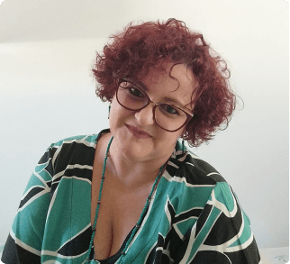 A imagem mostra a psicóloga Andéia Taufner com cabelo ruivo encaracolado, usando óculos e uma blusa verde e preta. Ela está sorrindo para a câmera.